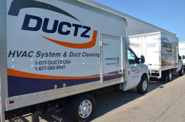 Two DUCTZ company vans parked on the side of a building.