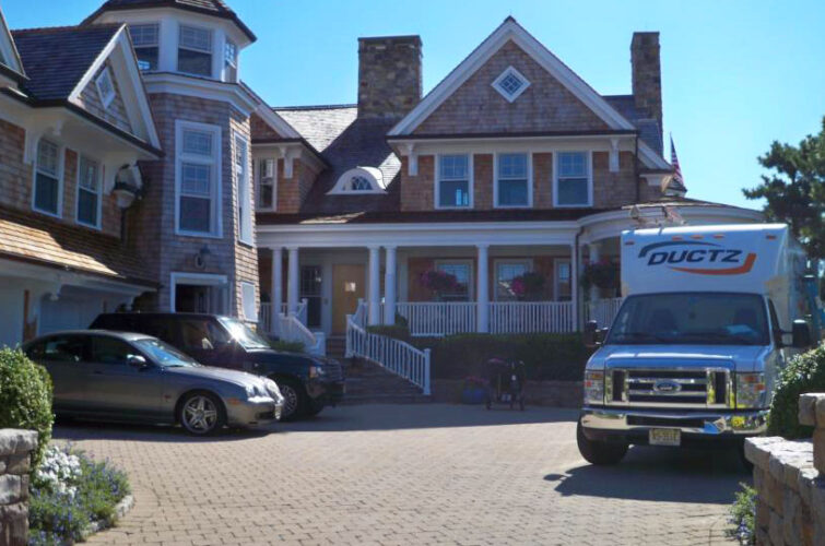 A DUCTZ company truck parked on the driveway of a large residential home.