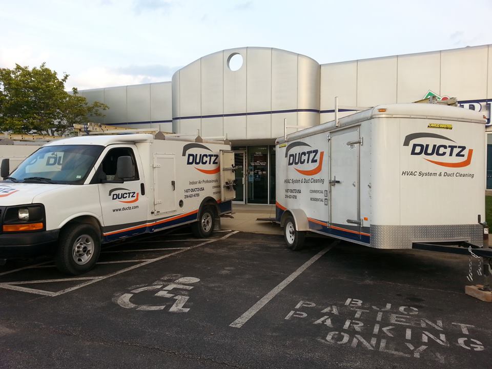 A DUCTZ commercial truck and trailer parked in the front of a commercial building.