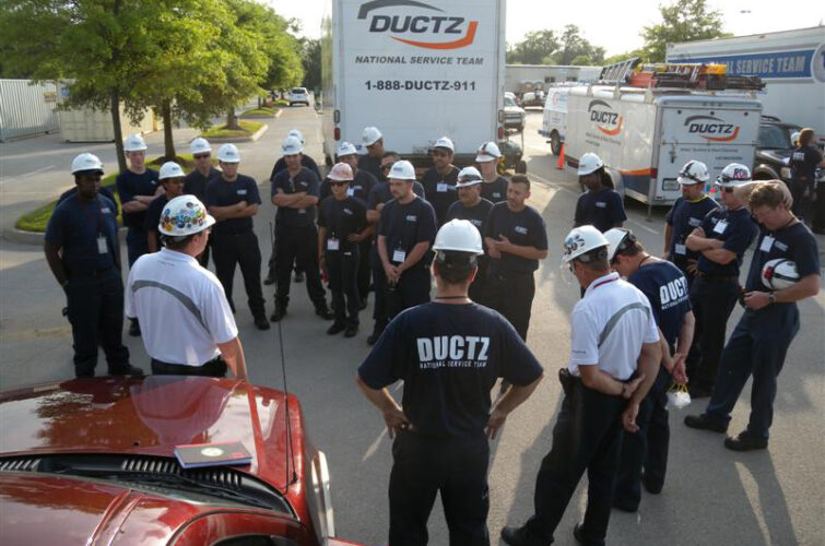 A group of DUCTZ workers huddling outside with DUCTZ service vehicles in the background.