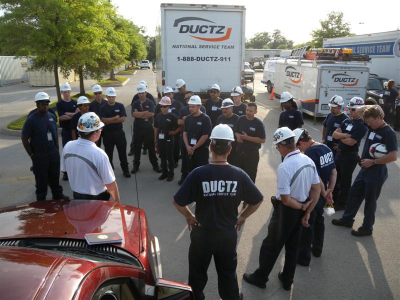 A group of DUCTZ workers huddling outside with DUCTZ service vehicles in the background.