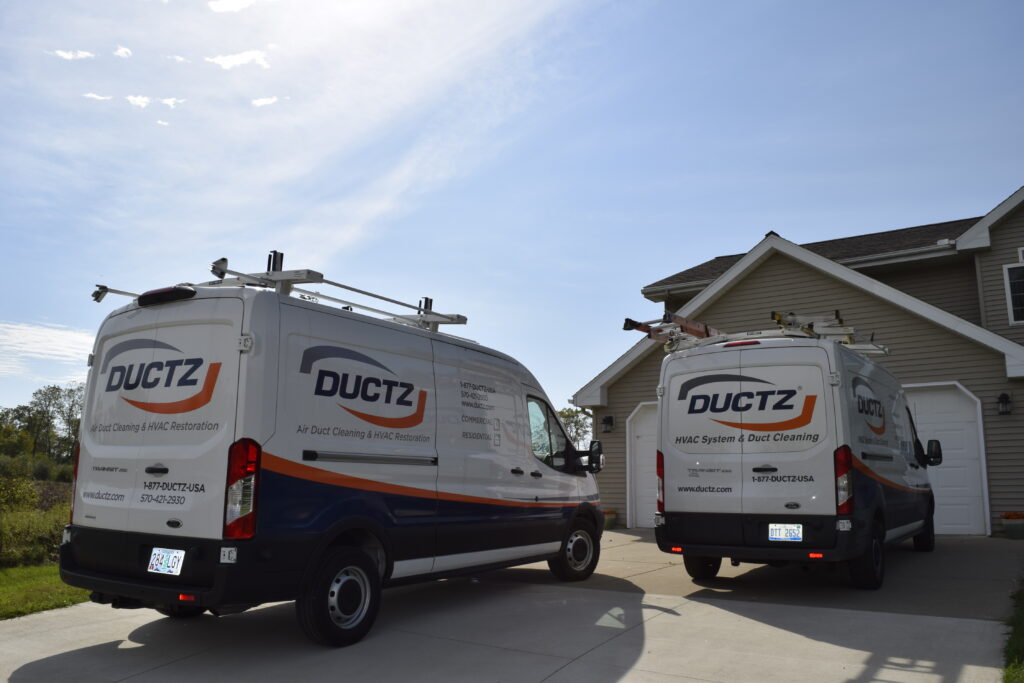 View of two DUCTZ vans parked in the driveway of a large residential home.
