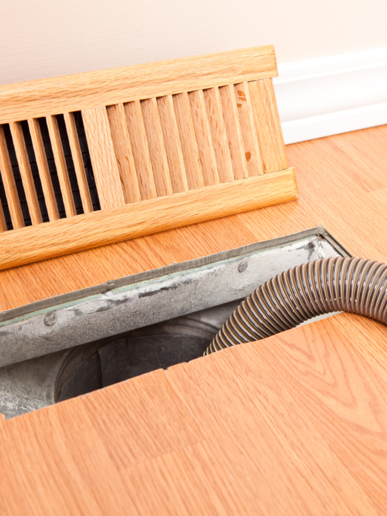 View of a residential home ground air duct vent with cleaning tools inside.